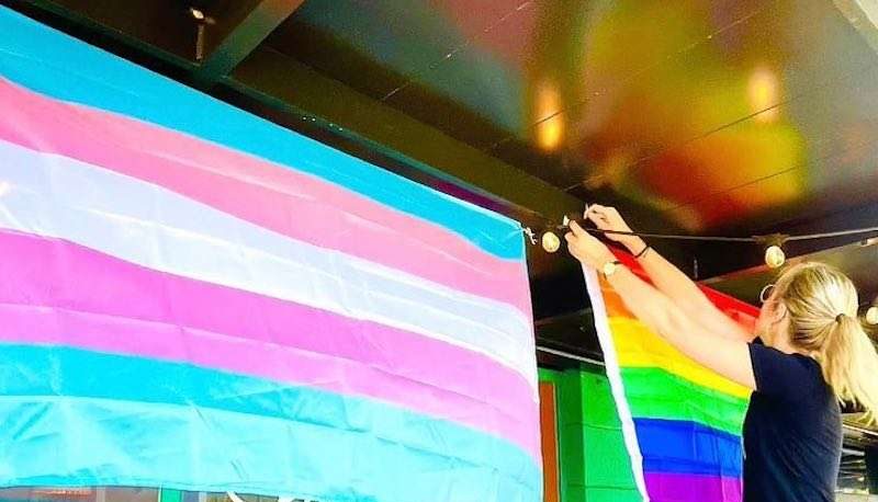 love food central pride — a person putting a pride flag and a trans flag on the building. (LGBTQ Businesses South Pinellas)