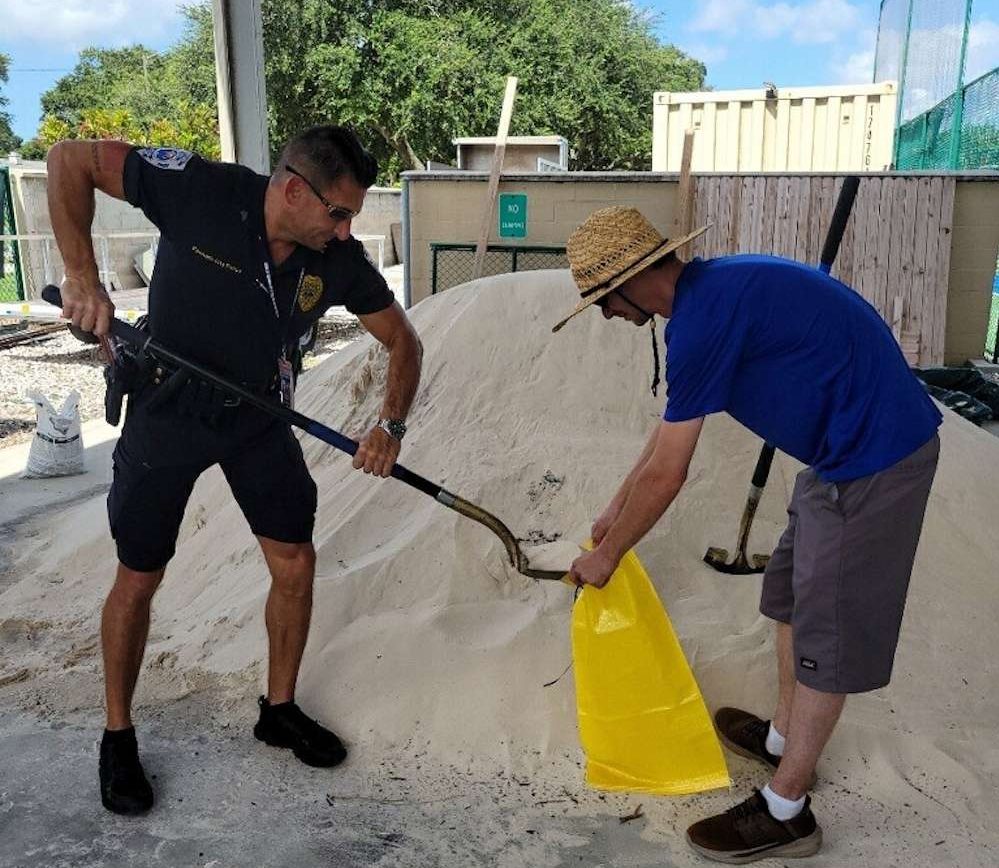 a cop shoveling sand into a yellow bag that a man holds open.