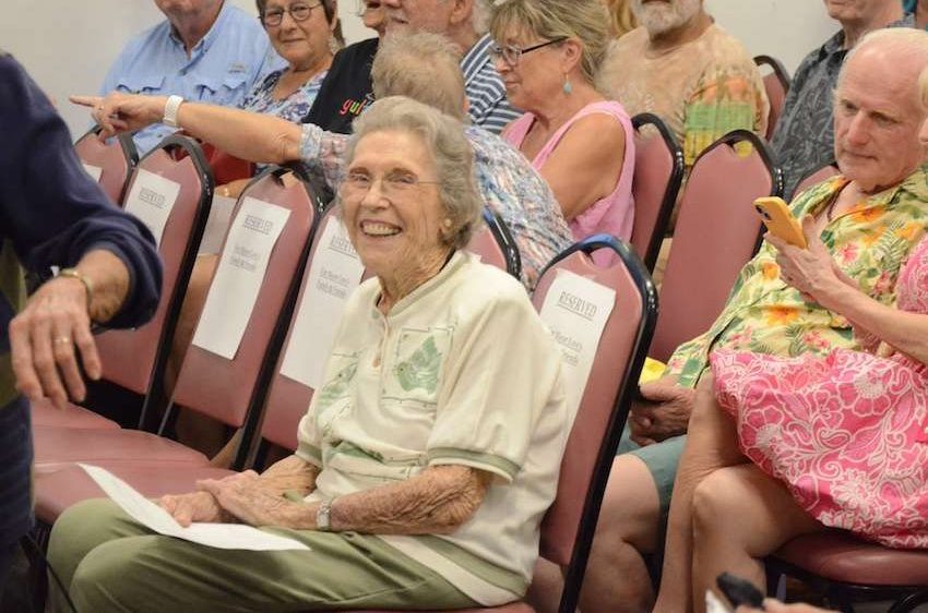 a woman smiling in her seat at a crowded council meeting.