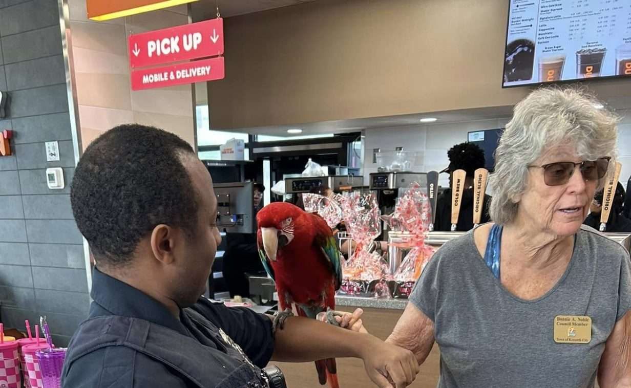 A police officer with a parrot on his arm and a lady with a nametag helping him hold the bird