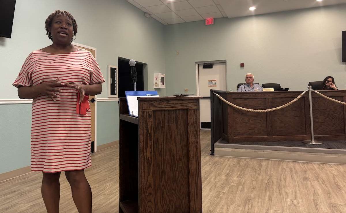 A woman standing in front of a podium while speaking to people in city hall.