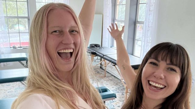 Two women, one blonde, one brunette, look happy inside a studio.