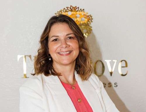 Woman with brown hair, pink shirt and white jacket.