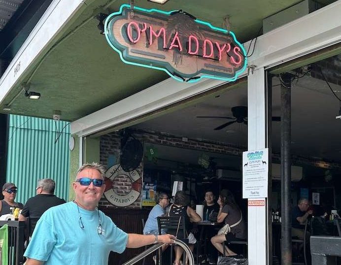 A man standing underneath an O'Maddy's sign.