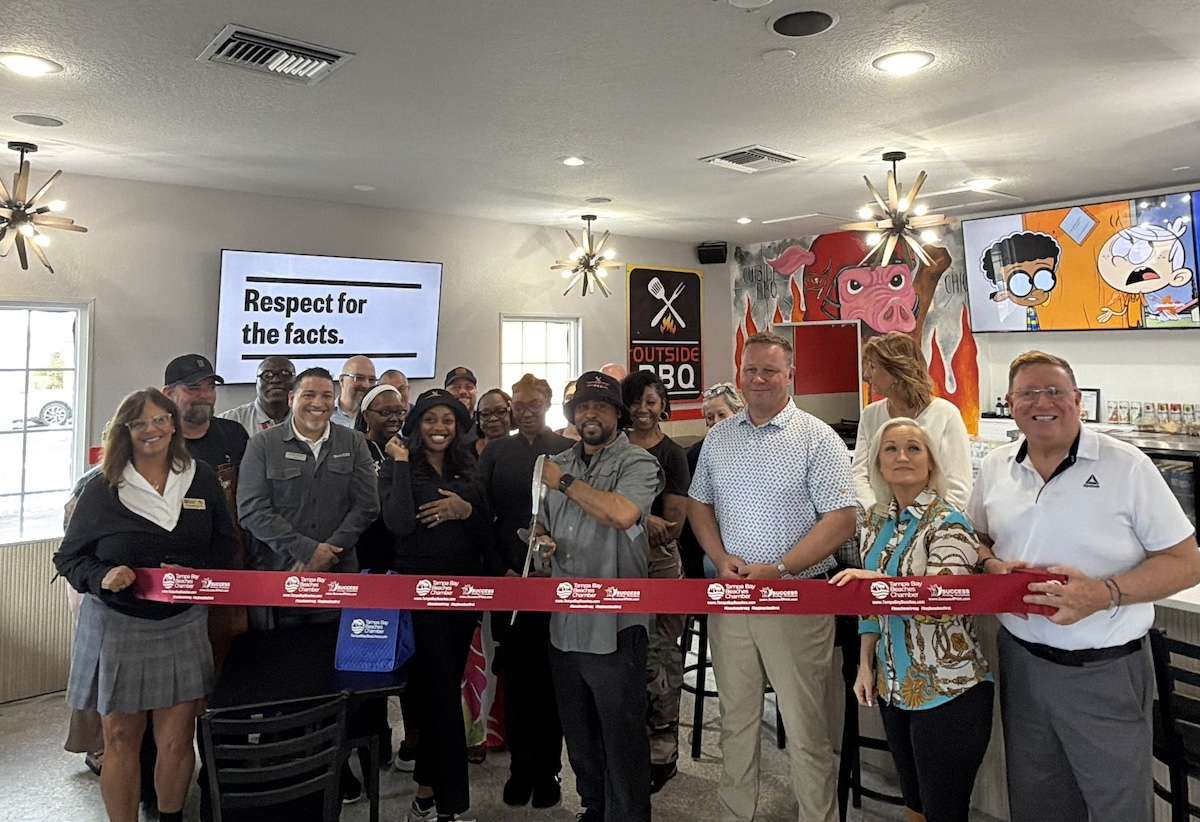 a group of people in a restaurant with a red ribbon and large scissors.