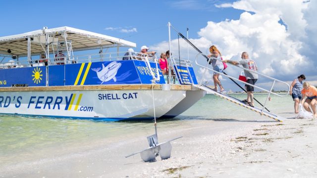 A boat on the sand with passengers boarding it.