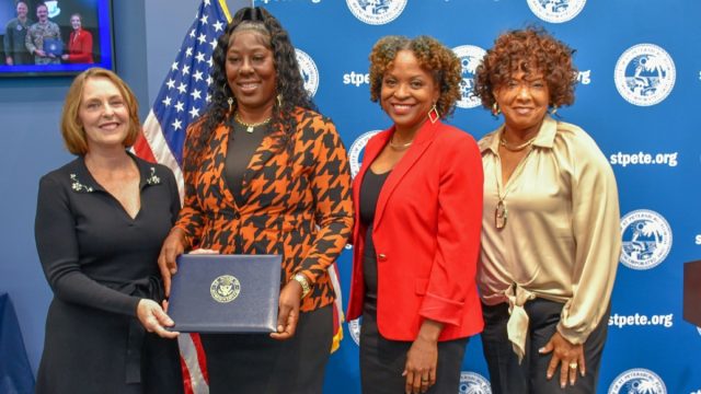 four women standing together while one woman holds a blue award.