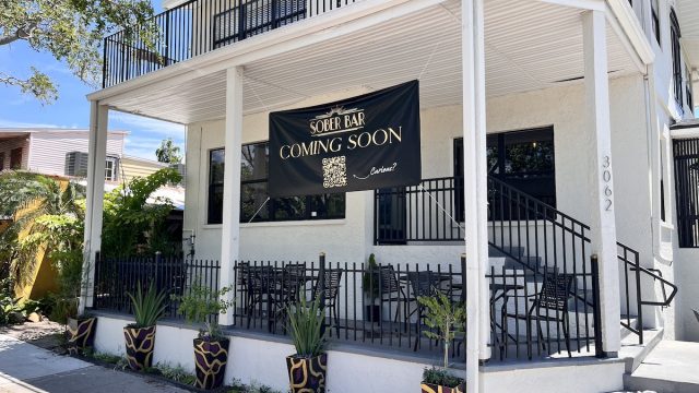 a white and black building with tables and chairs outside and a sign that reads 