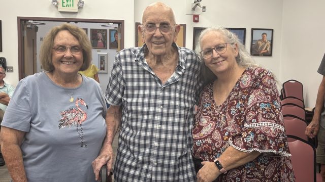 An elderly man with his daughters standing on either side of him.