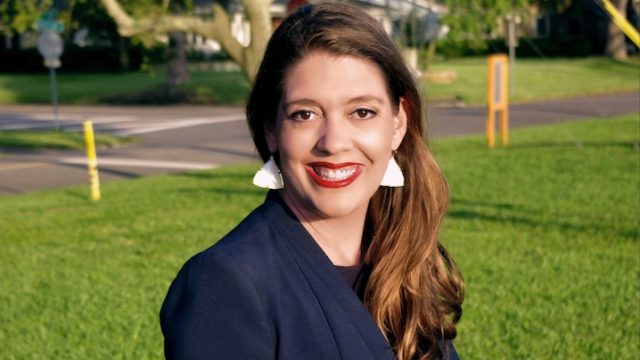 a woman smiling while sitting in front of grass.