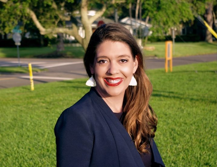 a woman smiling while sitting in front of grass.