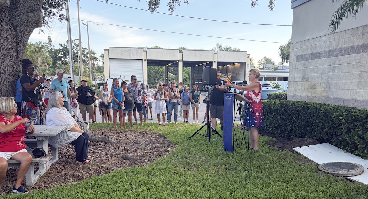 people standing outside and a woman speaking into a mic.