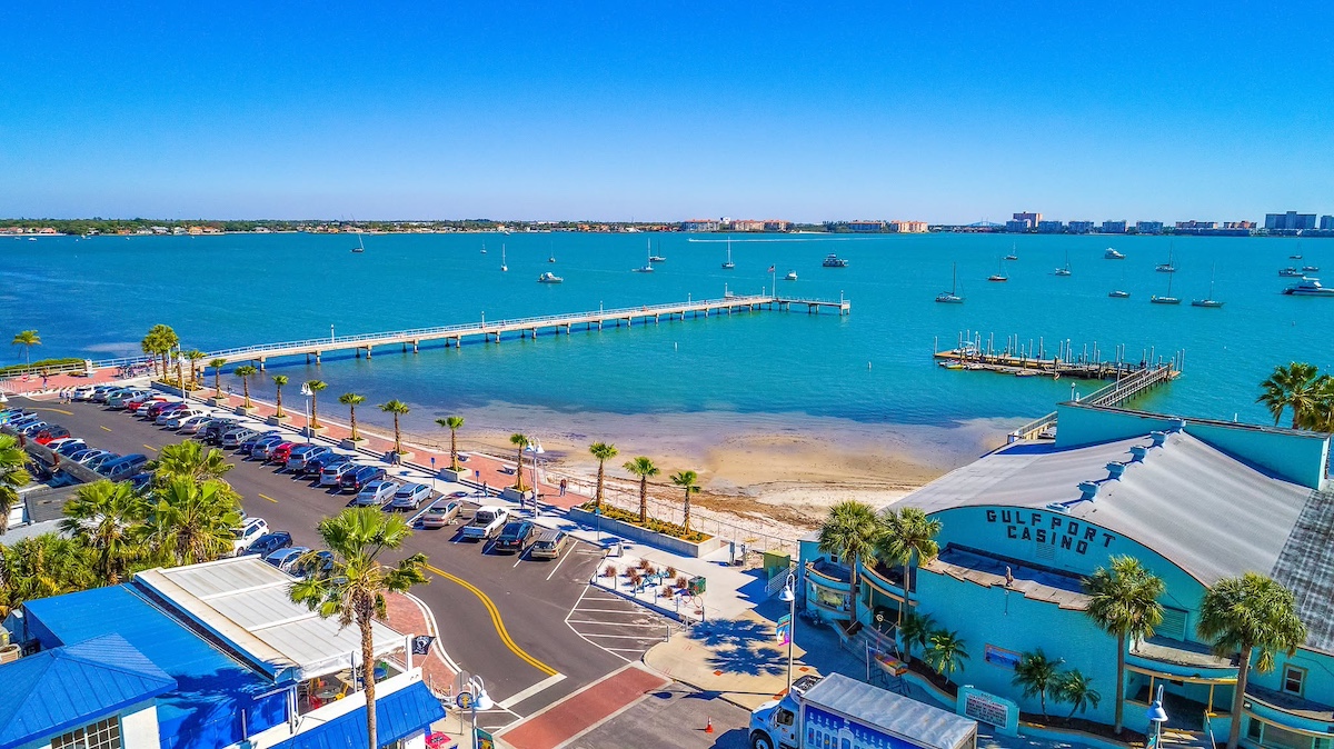 an aerial view of a bay next to a town with cars parked and a pier.