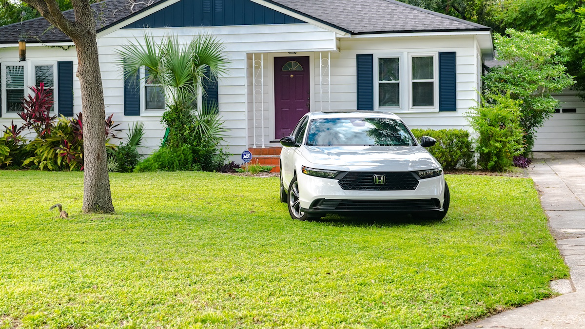 Clean white car parked on grass in front of charming white house with purple door