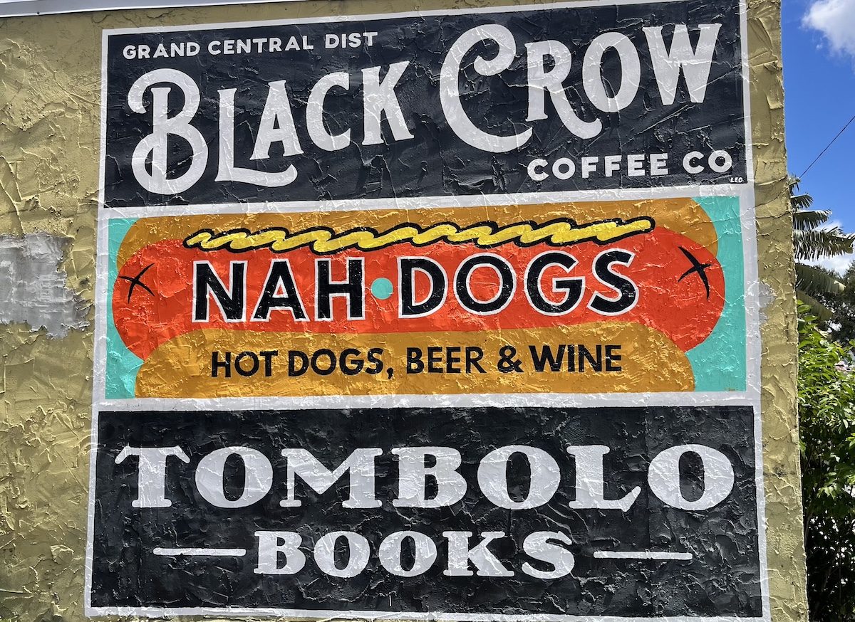 a mural of three businesses that read "black crow coffee, nah dogs, hot dogs, beer and wine, tombolo books"