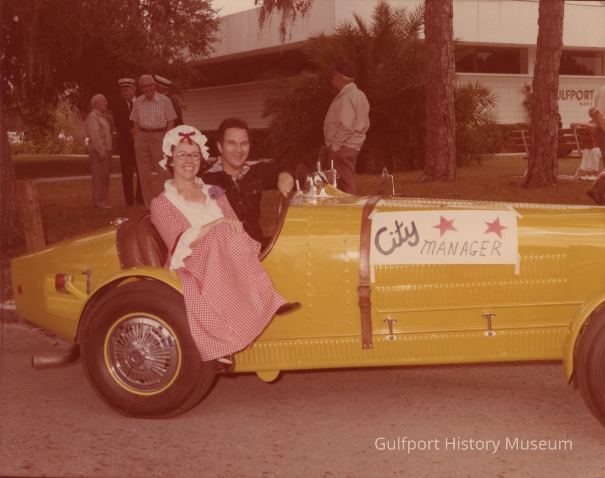 two people in a yellow car with a sign that reads "City Manager"